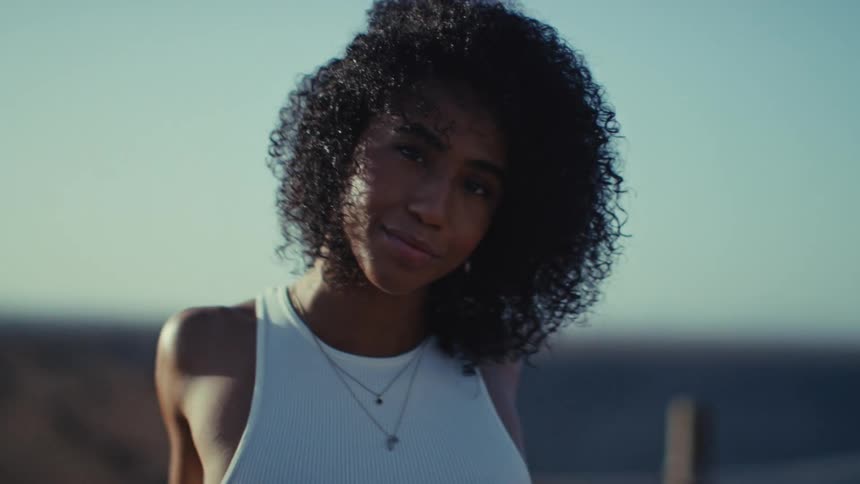Woman faces the camera outdoors with the ocean blurred in the background