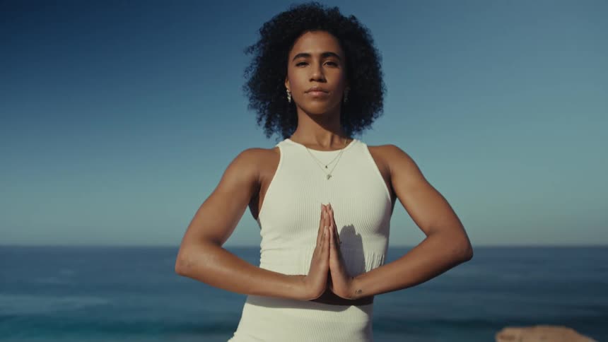 Woman standing with her hands together as she meditates along the coast