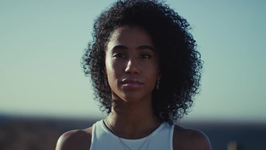 A woman looks directly at the camera in natural outdoor light with a blurred background
