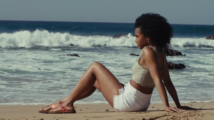 Woman wearing shorts and a sleeveless midriff baring shirt suns on the beach on a windy summer day