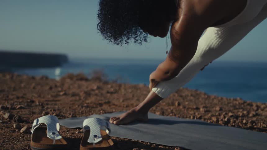 A young woman performs stretching exercises on an exercise mat on an ocean shore