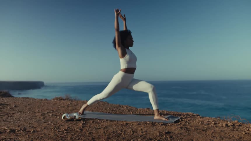 Woman performs a stretching pose on a cliff with the ocean in the background