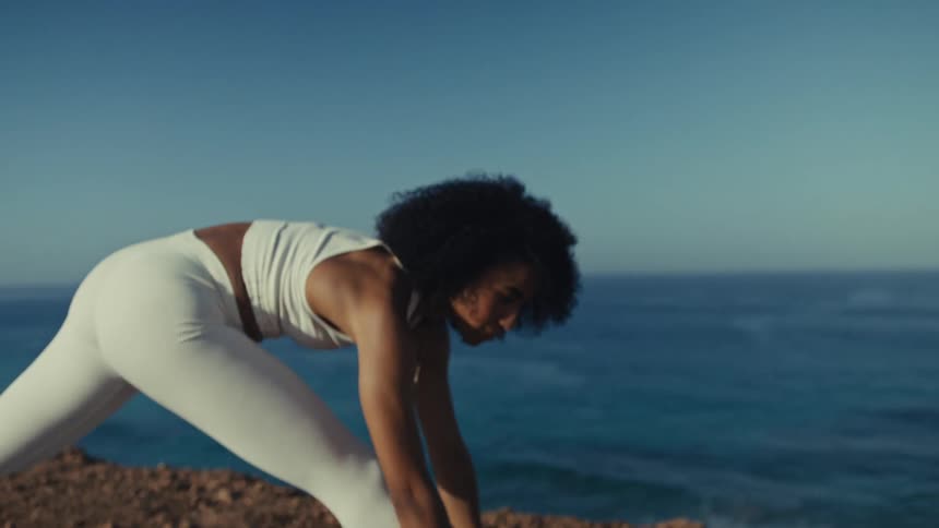 Woman stretching on a training mat on a cliff with the ocean in the background