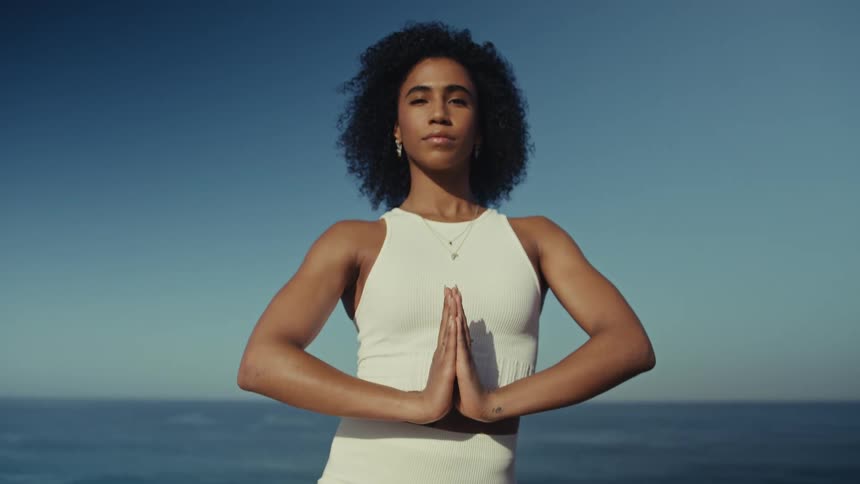 Woman performs a yoga pose with hands together facing the ocean