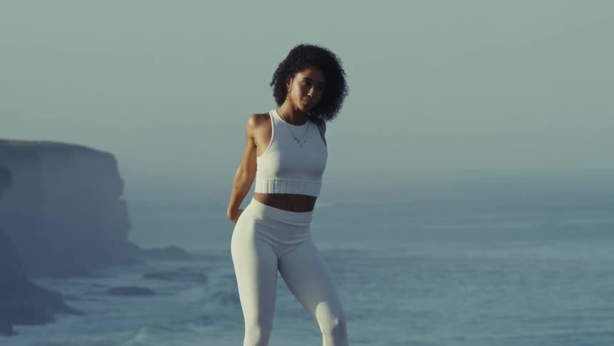 Woman stretching her arms overhead on a cliff edge with the ocean in the background