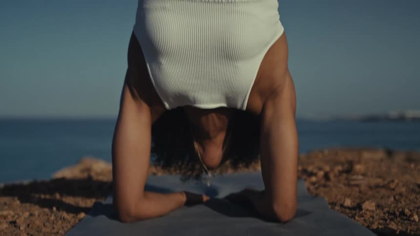Woman balancing upside down on her arms as she exercises along the coast