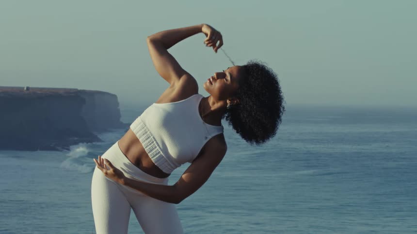 Woman performing a side stretch on a cliff edge with the ocean in the background