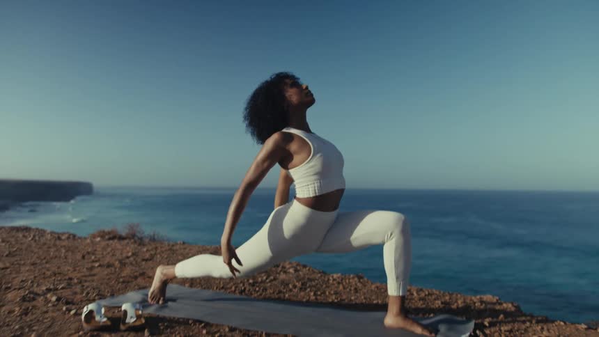 A woman gracefully moves through a series of yoga poses on a mat atop a seaside cliff her body strong and serene against the vast blue ocean backdrop