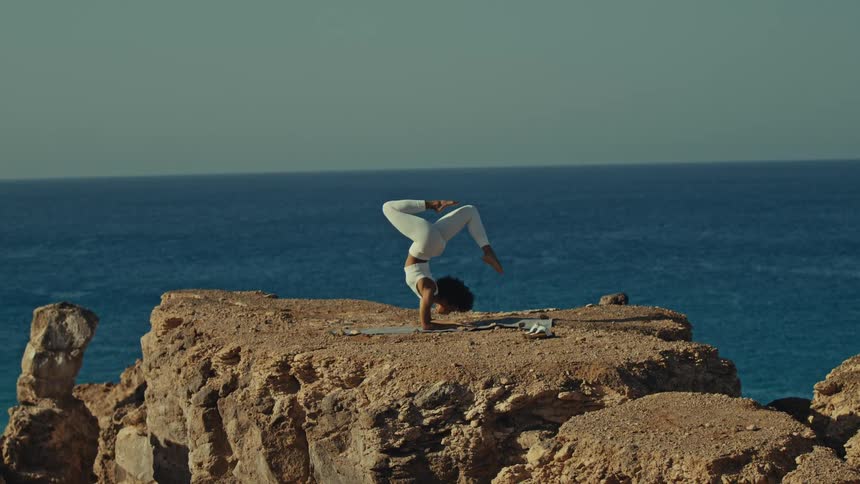 Woman balances on her forearms while performing yoga on a rocky shore during the daytime