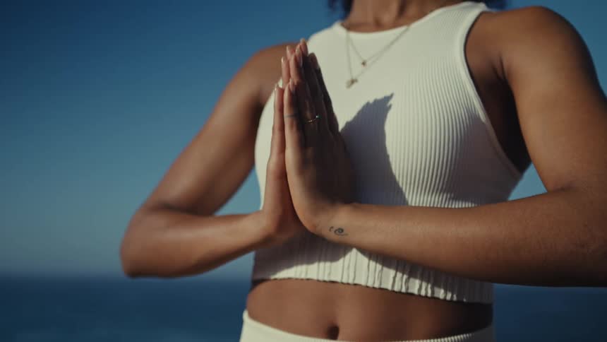 Woman takes a yoga pose while standing at the coast on a sunny summer day