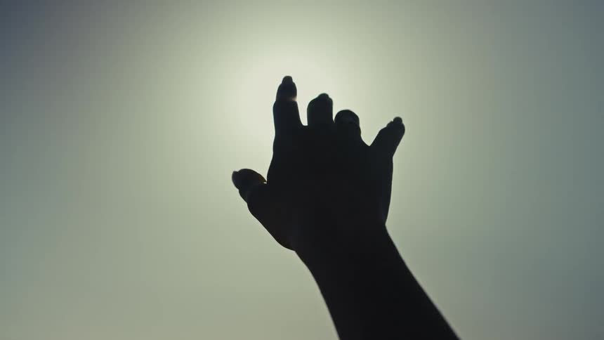 Female human hand reaching out towards the sun on the sky outdoors during day time