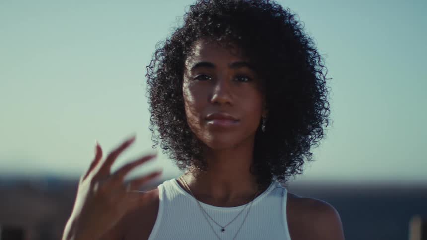 Woman with curly hair touching her face in an outdoor setting with the sky in the background