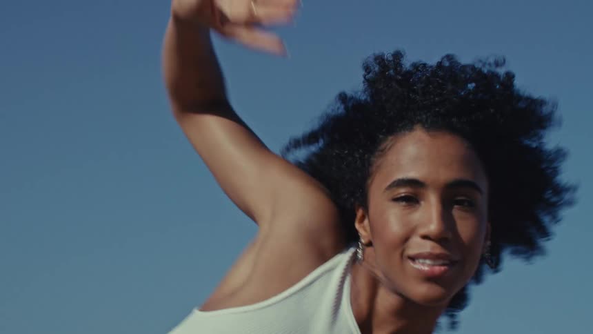 Young adult black woman dancing and moving her arms outdoors during day time
