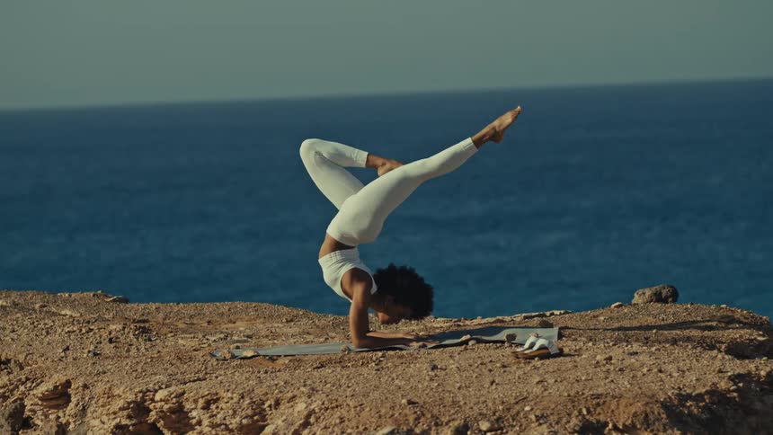 Woman balancing upside down on her arms as she exercises along the coast