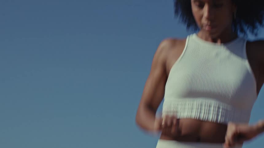 A young black woman wearing a white active shirt and yoga pants shows off a confident dance move at midday