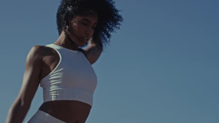 An athletic woman moves with graceful and powerful energy dancing and stretching freely against the vast expanse of a clear blue sky