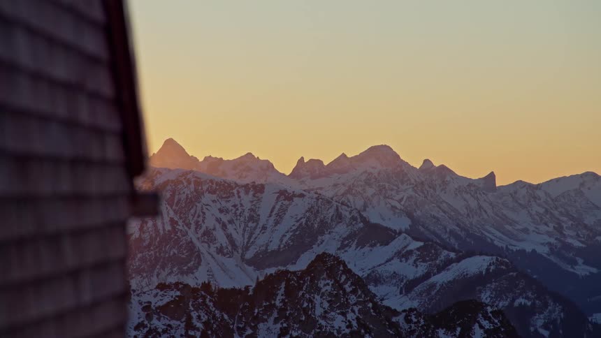 Snowcovered mountain range under dawn light seen beside an architectural structure