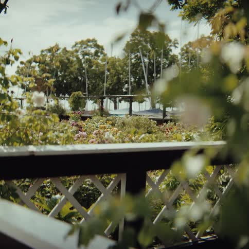 Flowered garden seen through a white railing with trees in the background and a suspended structure among them
