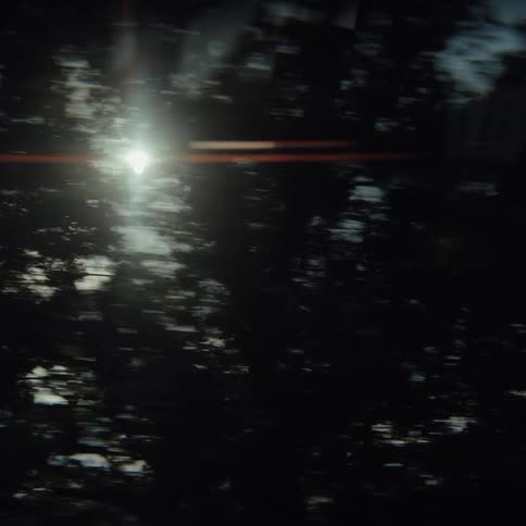 A view from a moving vehicle shows dark blurred trees passing by before transitioning to a bright sunlit sky with scattered white clouds and the tops of green trees