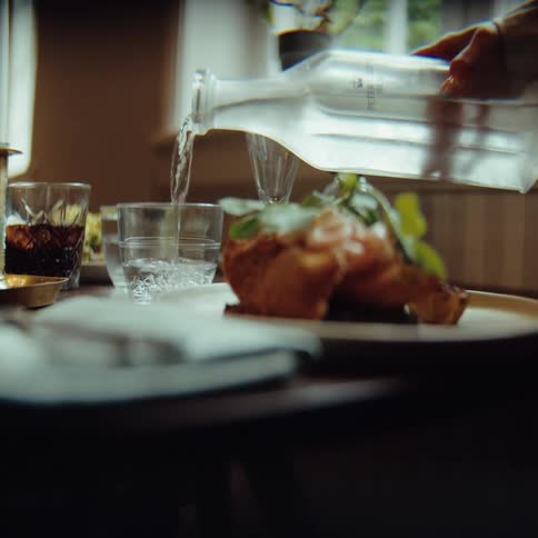 Water being poured from a glass bottle into a cup on a table with food