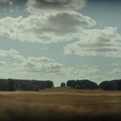 The video captures a scenic view of rolling golden fields and distant woodlands under a cloudy sky likely taken from a moving vehicle as the camera travels the open landscape quickly transitions into a blur of dense green trees passing close by