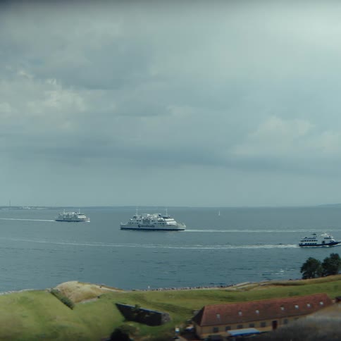 Vessels sail on open water near the coastline under a cloudy sky