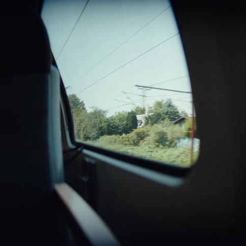 The video shows a view of the passing landscape from a train window as it travels through a suburban or rural area lush green trees and residential buildings move quickly across the frame under a clear blue sky