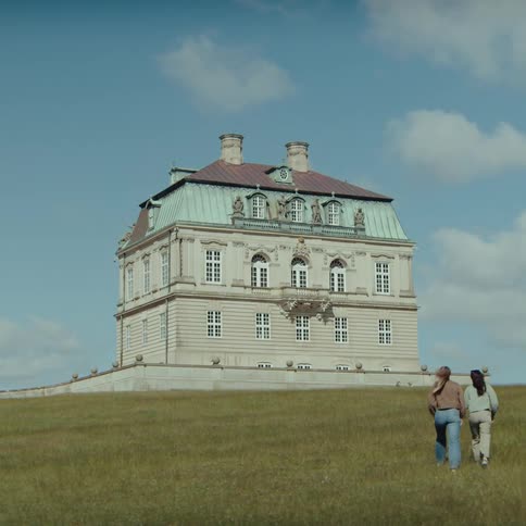 Historic building isolated on a grassy hill with people walking toward the structure