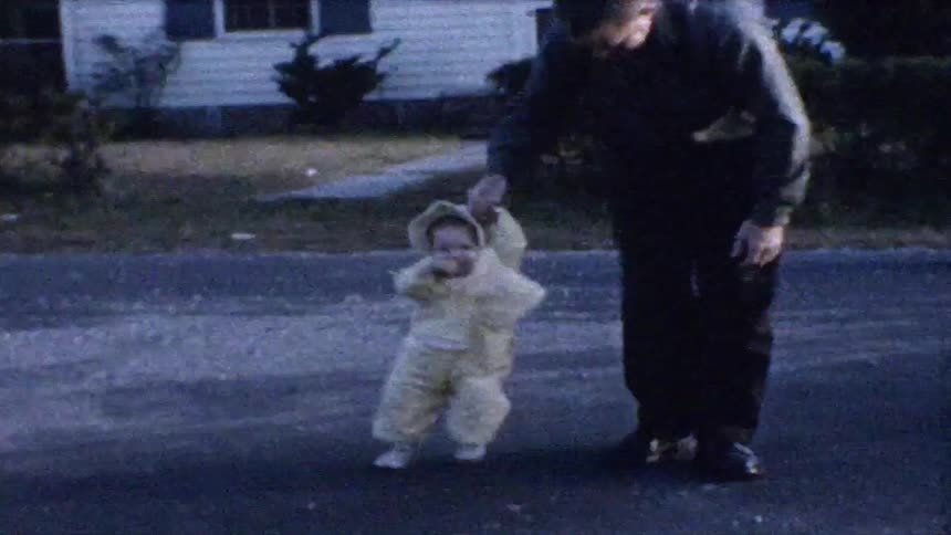 An elderly man is holding the hand of a small child walking next to him on a street in front of a house