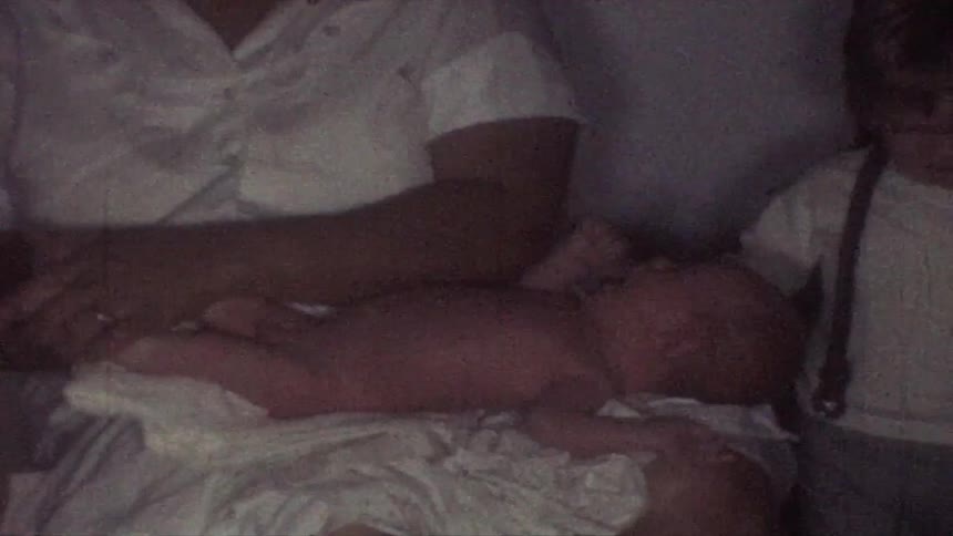 A mother gently taking care of infant on her lap while a young child sits beside her indoors
