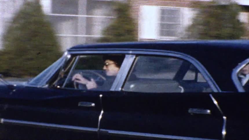 Person driving a vintage car in a residential area with houses in the background