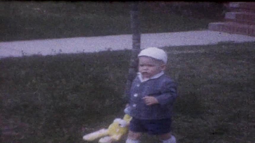 Small toddler boy walking around a yard carrying a yellow toy on his hand outdoors during day time