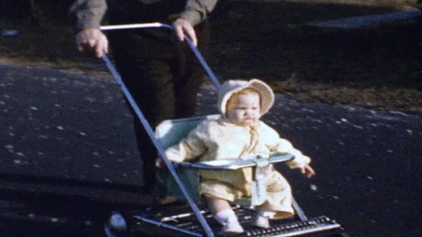 A man pushes a baby in a vintage stroller along a paved outdoor path