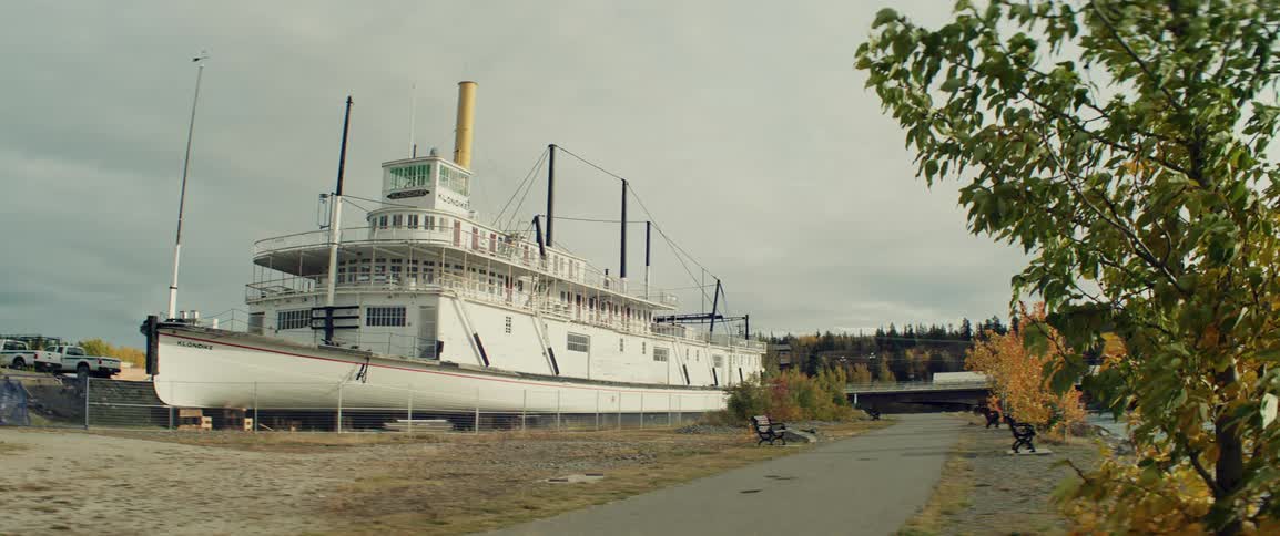 A historic white steamship rests on dry land beside a paved walking path under an overcast sky