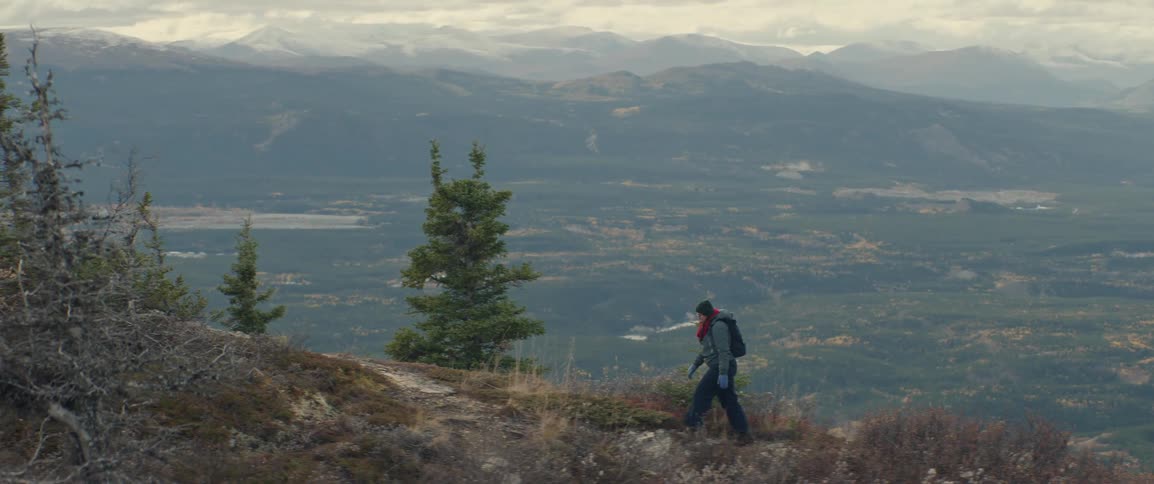 Person walking along a ridge trail overlooking a broad valley and distant mountains