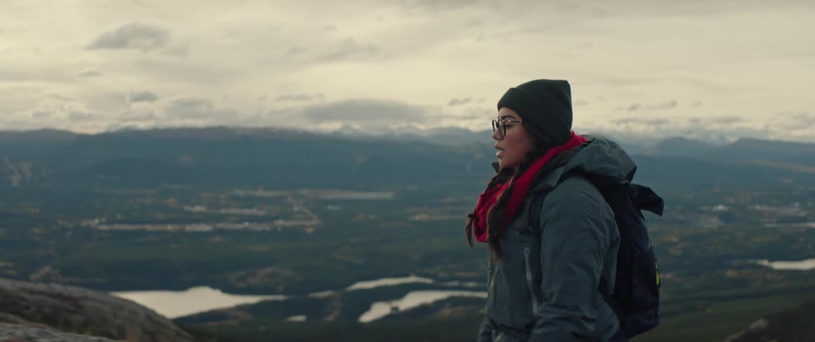 A person wearing winter gear and a backpack reaches the summit of a mountain looking out over a rugged valley