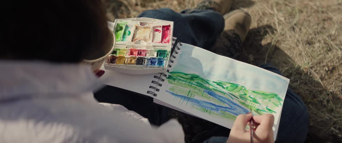 Person painting a landscape in a sketchbook with watercolors outdoors