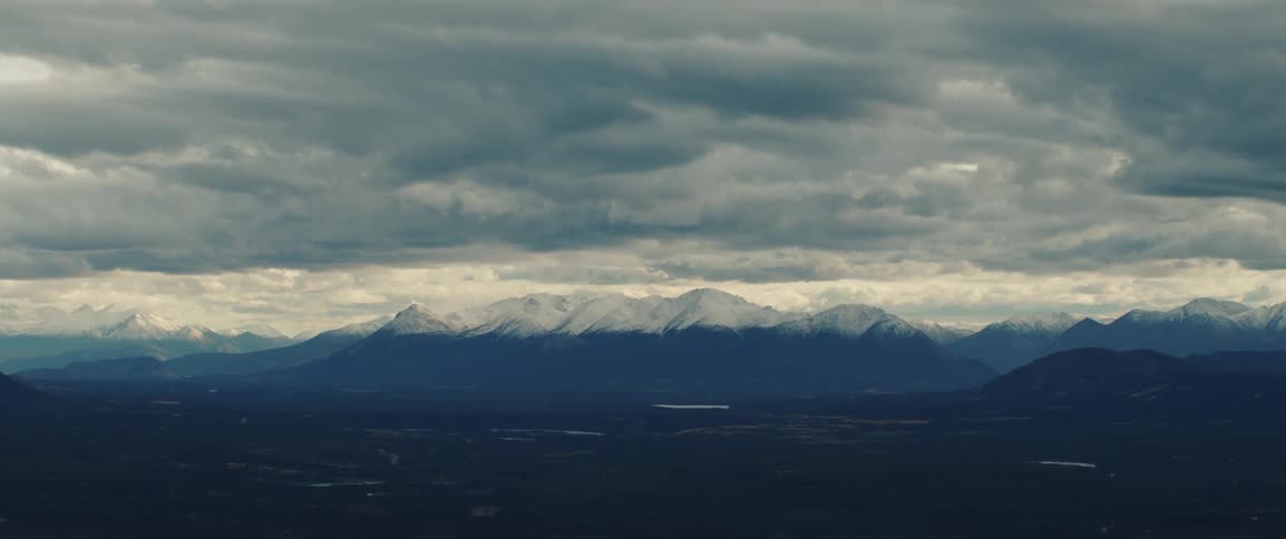 A cloudy day settles over the mountains and the peakcovered in snowcatches the last light of sunset as the sky glows behind the drifting clouds