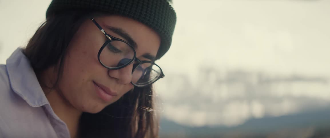 Woman wearing a beanie and glasses looking down at her work while she paints a landscape