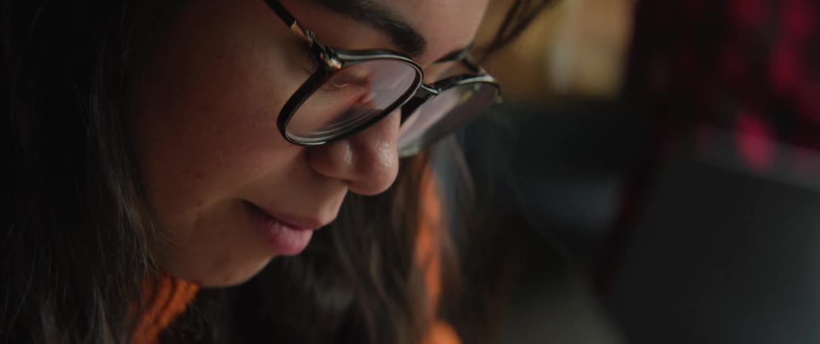 A woman with dark hair and glasses looks down with a focused expression