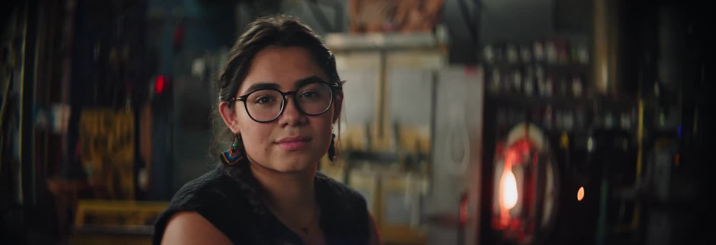 A woman wearing glasses in a workshop smiles at the camera