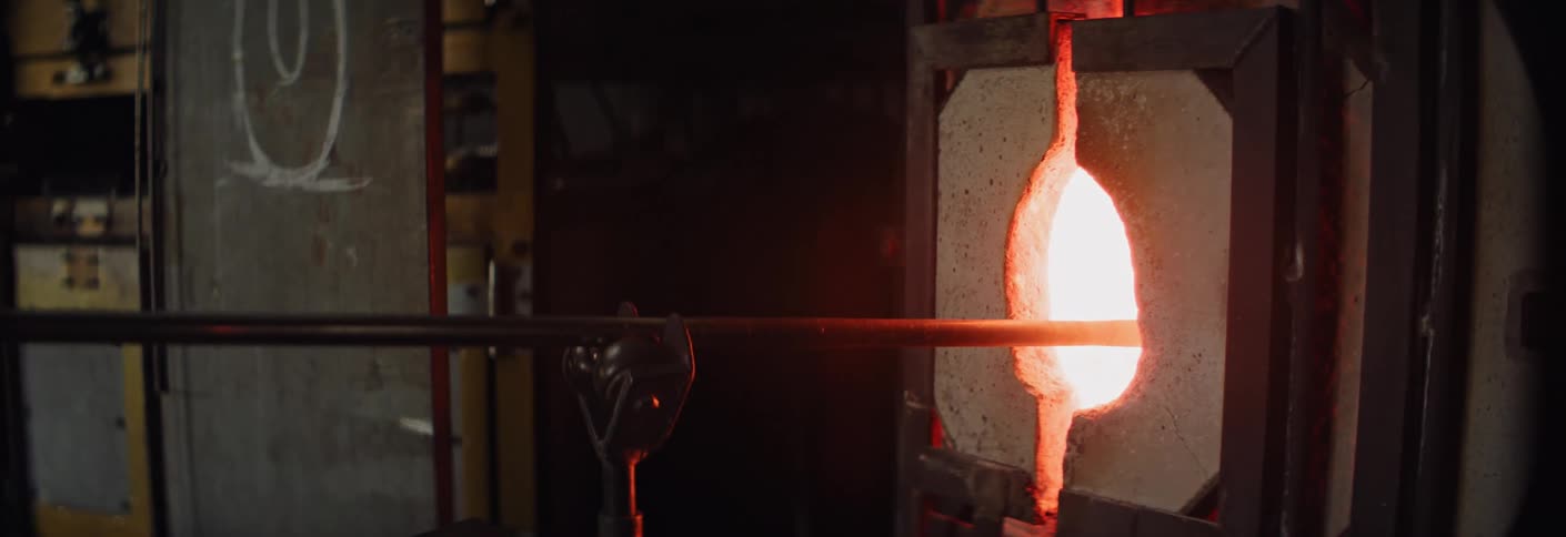 Heated glass being shaped in an industrial furnace with a glowing opening