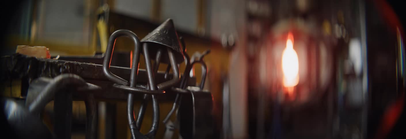 Metal tools hang near on a rack in front of a burning furnace