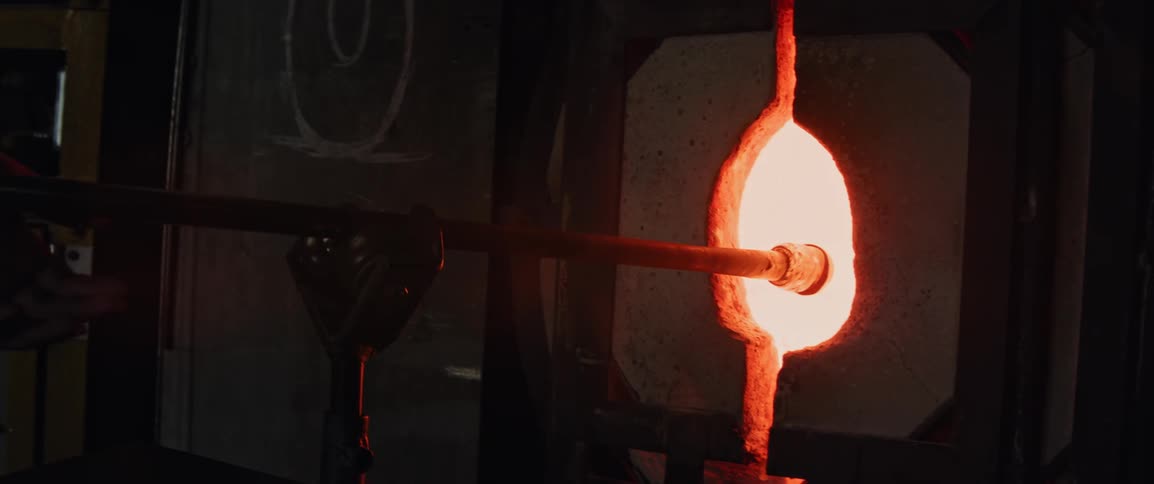 The glass blower rolls the molten material to form its shape