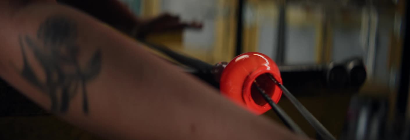 Molten glass being shaped with a metal tool in a glassblowing workshop