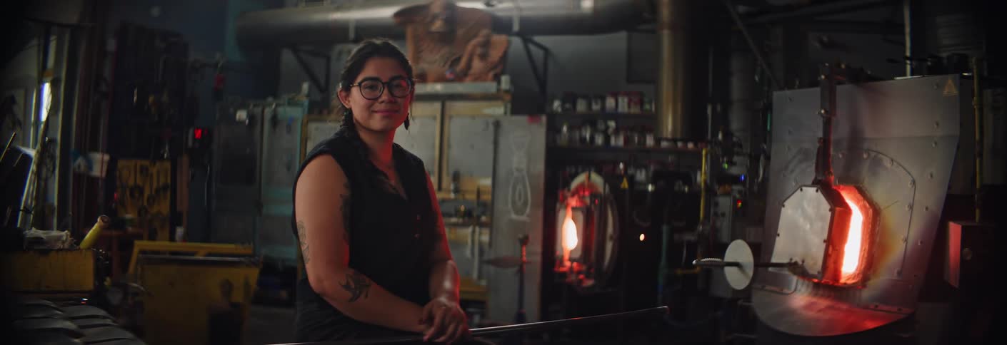 Portrait of a woman in a glass blowing workshop surrounded by industrial furnaces