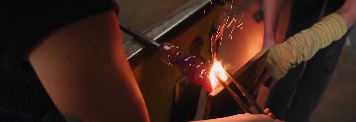 Two glass blowers working to shape a glass vase