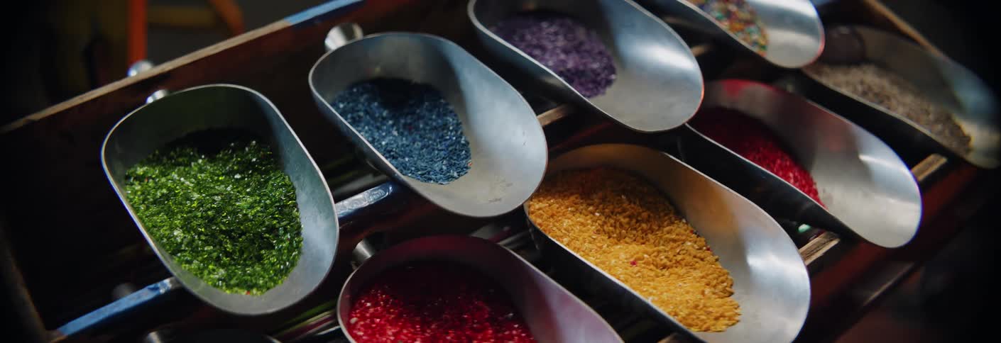 Metal scoops holding colored glass fragments organized for glassblowing