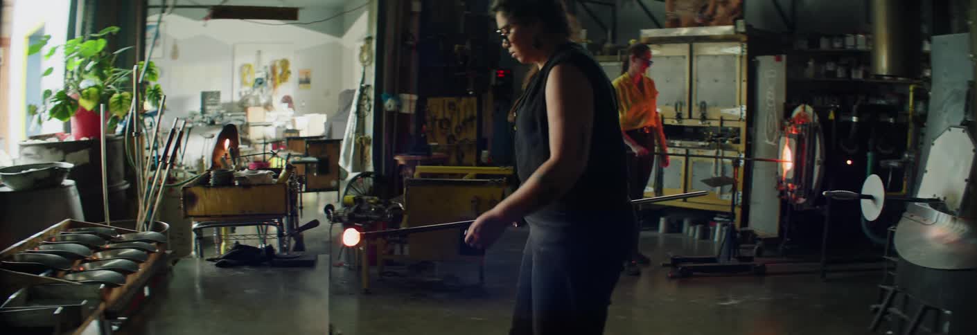 Workers handling molten glass in a furnace inside a glassblowing workshop