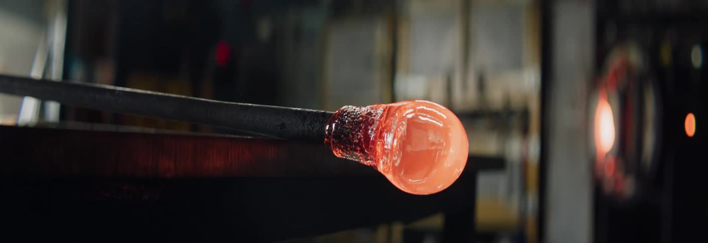 A glass bubble is seen forming on the end of a metal rod in a workshop